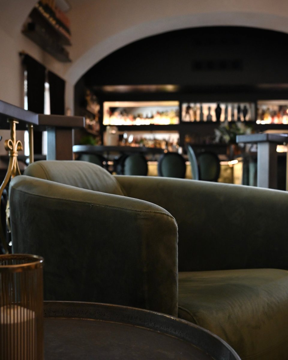 Grüner Samtsessel in der Josef Cocktailbar, dahinter die beleuchtete Bar unter dem Gewölbe